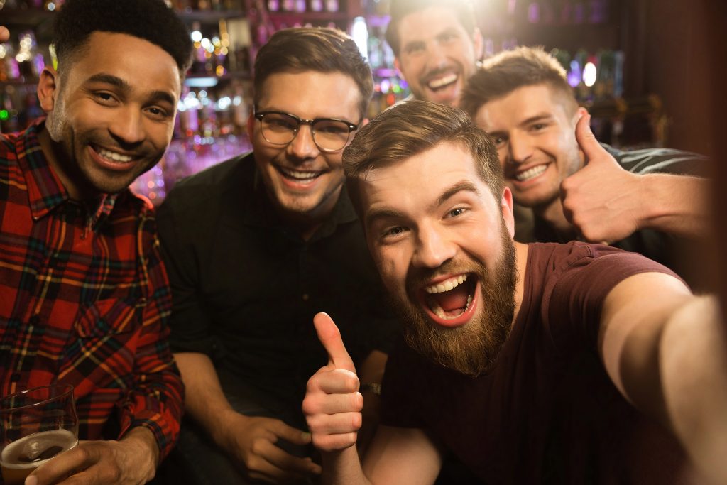 Cheerful old friends having fun by taking selfie and drinking draft beer in pub
